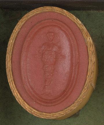 czerwona owalna gemma w grubym złotym obramowaniu; kobieta widziana na wprost stojąca prosto z rozportartymi rękami; jest ubrana w bardzo bogaty i nietypowy strój, kobieta ma naszyjnik, na wysokości dekoracja w kształcie ptasich jaj lub wielu samskich piersi, poniżej ułożone w poziomych rzędach przedstawienia zwierząt