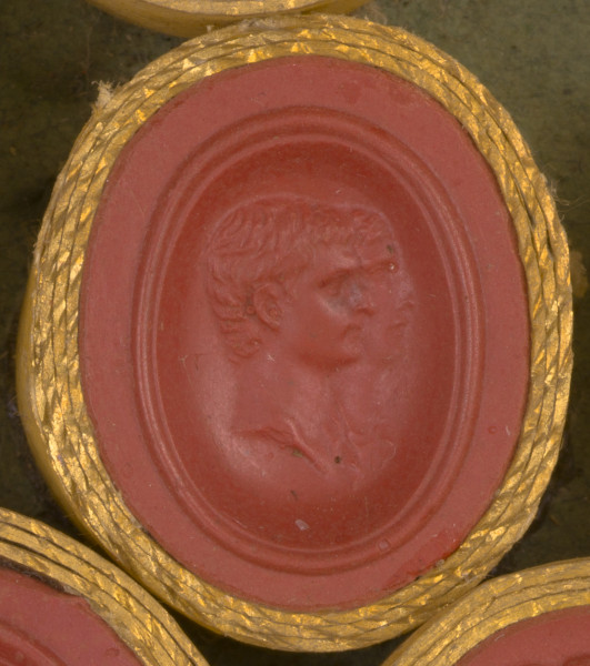 czerwona gemma, owalna pionowa, w grubym złotym obramowaniu. Dwa nakładające się na siebie prawe profile: młodego mężczyzny i kobiety. Mężczyzna o krótkich włosach i lekko garbatym nosie, za nim nieco schowana kobieta o prostym nosie.