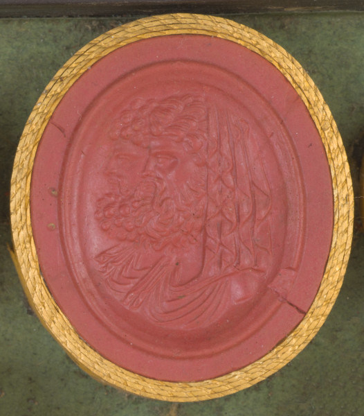 czerwona owalna gemma w grubym złotym obramowaniu; dwaj mężczyźni ukazani do wysokości piersi, na pierwszym planie mężczyzna z kręconymi włosami okrytymi udrapowaną chustą oraz z bujną, kręconą brodą; na drugim planie mężczyzna z kręconymi włosami i brodą; na ramionach obydwu mężczyzn widoczne udrapowanie tuniki