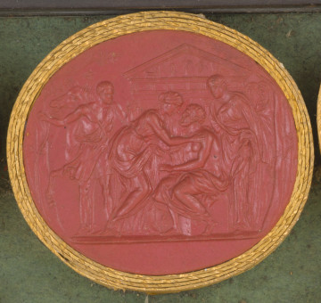 czerwona owalna gemma w grubym złotym obramowaniu; scena przedstawia 6 osób ubranych w stroje antyczne; na pierwszym planie siedzi oślepiony starszy mężczyzna (Edyp), w którego stronę pochyla się młoda kobieta (Antygona); za Edypem stoi młoda kobieta (Ismena). Z lewej strony widoczny jest młody mężczyzna trzymający konia za uzdę. Na dalszym planie widać dwóch kapłanów, a w tle fasadę świątyni