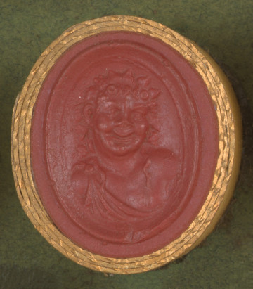 czerwona owalna gemma w grubym złotym obramowaniu; popiersie młodego uśmiechniętego fauna w wieńcu z winorośli z długimi włosami opadającymi na ramiona, ubrany w tunikę zapiętą na jednym ramieniu; 