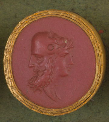 czerwona okrągła gemma w grubym złotym obramowaniu; trzy połączone ze sobą twarze: po lewej stronie profil twarzy brodatego starca, po prawej młodzieńca. U góry obie twarze łączy trupia czaszka leżąca poziomo, czoło starca i czoło czaszki są wspólne. Broda czaszki przechodzi we włosy nad czołem młodzieńca