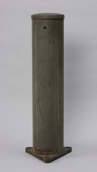 Systemowe Urządzenie Sygnalizacyjne - Ujęcie z tyłu; Urządzenie sygnalizacyjne będące fragmentem systemu ochrony granic PRL. Składa się z dwóch metalowych słupów, w których zamontowano czujniki na podczerwień. Każde z urządzeń znajduje się w obudowie o kształcie walca zamontowanej na trójkątnej podstawie. Zaopatrzone jest w dwie soczewki umieszczone jedna nad drugą.