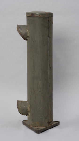 Systemowe Urządzenie Sygnalizacyjne - Ujęcie ze skosu z prawej strony; Urządzenie sygnalizacyjne będące fragmentem systemu ochrony granic PRL. Składa się z dwóch metalowych słupów, w których zamontowano czujniki na podczerwień. Każde z urządzeń znajduje się w obudowie o kształcie walca zamontowanej na trójkątnej podstawie. Zaopatrzone jest w dwie soczewki umieszczone jedna nad drugą.