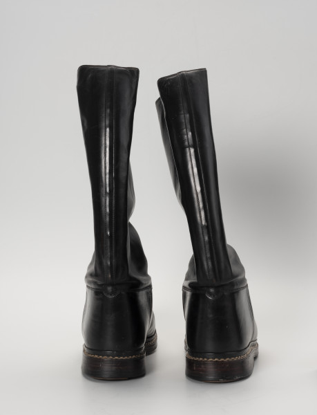 para butów oficerek - Ujęcie z tyłu; Para męskich, skórzanych butów z wysokimi cholewami, zrobionych na wzór oficerek przedwojennych. Przyszwy i cholewy wykonane z barwionej na czarno skóry, przyszyte dratwą do podeszwy podwójnymi szwami.