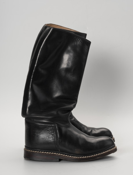 para butów oficerek - Ujęcie lewy bok; Para męskich, skórzanych butów z wysokimi cholewami, zrobionych na wzór oficerek przedwojennych. Przyszwy i cholewy wykonane z barwionej na czarno skóry, przyszyte dratwą do podeszwy podwójnymi szwami.