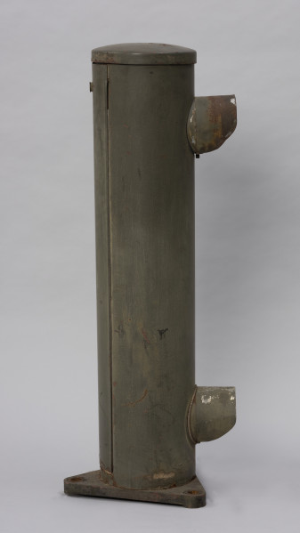 Systemowe Urządzenie Sygnalizacyjne - Ujęcie z lewej strony; Urządzenie sygnalizacyjne będące fragmentem systemu ochrony granic PRL. Składa się z dwóch metalowych słupów, w których zamontowano czujniki na podczerwień. Każde z urządzeń znajduje się w obudowie o kształcie walca zamontowanej na trójkątnej podstawie. Zaopatrzone jest w dwie soczewki umieszczone jedna nad drugą.