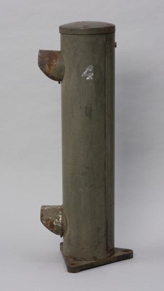 Systemowe Urządzenie Sygnalizacyjne - Ujęcie z prawej strony; Urządzenie sygnalizacyjne będące fragmentem systemu ochrony granic PRL. Składa się z dwóch metalowych słupów, w których zamontowano czujniki na podczerwień. Każde z urządzeń znajduje się w obudowie o kształcie walca zamontowanej na trójkątnej podstawie. Zaopatrzone jest w dwie soczewki umieszczone jedna nad drugą.