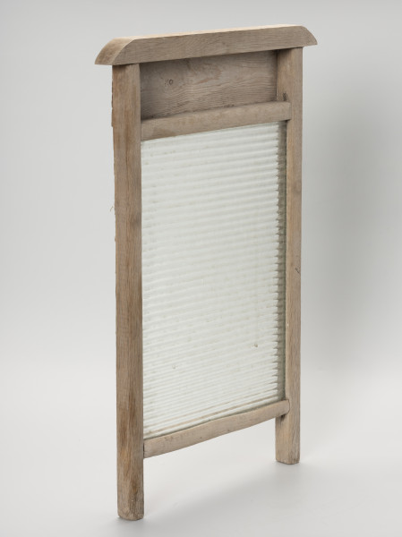 Tara do prania - ujęcie z ze skosu z lewej; Tara do prania złożona z prostokątnej, szklanej tafli osadzonej w drewnianej ramie. Szklana część jednostronnie karbowana. Oprawa z dwóch pionowych listew tworzących w dolnej części nóżki, dwóch poprzecznych listew stanowiących oparcie dla tafli oraz górnej profilowanej.