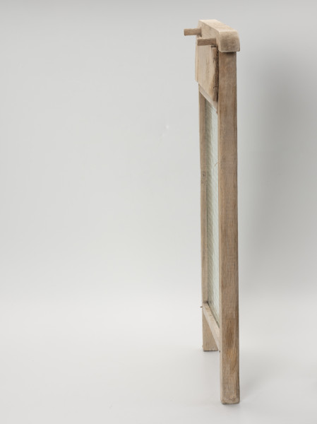 Tara do prania - prawy bok; Tara do prania osadzona w drewnianej ramie. Szklana część jednostronnie karbowana. Oprawa z dwóch pionowych listew tworzących w dolnej części nóżki, dwóch poprzecznych listew stanowiących oparcie dla tafli oraz górnej profilowanej z wystającymi końcówkami stanowiącymi uchwyt. Od tyłu, pomiędzy listwą uchwytową, a górną poprzeczką przybita prostokątna, cienka deska. Powyżej w listwie uchwytowej wkręcone dwa drewniane kołki wystające na lewo umożliwiające zawieszenie tary na brzegach balii.