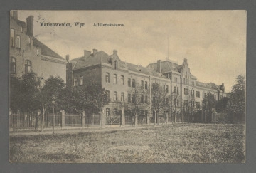 Pocztówka czarno biała, w kadrze poziomym. W lewym górnym rogu wydrukowany napis Marienwerder, Wpr. Artilleriekaserne. Pocztówka z widokiem architektury. Na pierwszym planie duża płaszczyzna porośnięta trawą. Dalej ceglano metalowe ogrodzenie z metalową bramą wjazdową pośrodku. Bezpośrednio za ogrodzeniem wysokie drzewa z rozłożystymi, ulistwionymi koronami, a za nimi ciąg budynków z cegły w stylu neogotyckim, ze spadzistymi dachami. Budynek z lewej strony widoczny tylko częściowo. Obok niego podłużny, dwupiętrowy budynek, w części środkowej podwyższony, zwieńczony schodkowym szczytem. W tej części dach jest czterospadowy, na górze płasko ścięty, obwiedziony barierką, z wysokim masztem na flagę pośrodku. Na każdej kondygnacji budynku regularnie rozmieszczone, duże, prostokątne okna, zakończone lekkim łukiem, wypełniające większą część ścian. Na dachu widoczne małe okienka.