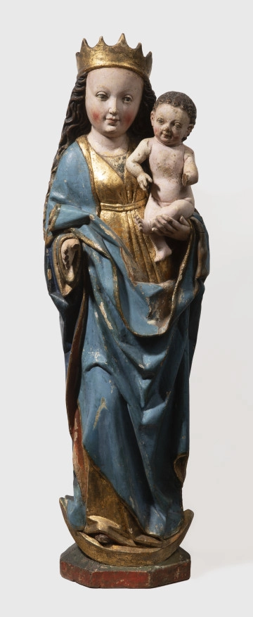 MZM/Rz/84 Fotografia kolorowa. Figura drewniana, malowana, przedstawiająca Madonnę z Dzieciątkiem stojącą na złotym półksiężycu. Całość na niskiej, wielobocznej podstawie. Kobieta ubrana w długą, złotą suknię i narzucony na ramiona błękitny płaszcz, który udrapowany w fałdy spływa do ziemi, ukazując na dole, po prawej stronie tylko kawałek sukni. Na głowie złota, otwarta korona. Włosy długie, ciemne z wyraźnymi falowaniami, spadające na plecy. Czoło wysokie, bez włosów. Brwi bardzo delikatnie zarysowane, oczy małe, otwarte. Nos mały, usta pełne, niewielkie. Policzki mocno zaznaczone czerwonym kolorem. Prawą, otwartą, wyłaniającą się z fałd szaty dłoń ma wyciągniętą do przodu tak jak w geście powitania. Na lewym ręku trzyma małe nagie dziecko. Prawa nóżka dziecka zwisa swobodnie, lewa jest podkurczona i podtrzymywana dłonią kobiety. Prawa rączka dziecka opiera się o pierś kobiety, lewa jest zgięta i wyciągnięta do przodu. Brak dłoni. Głowa dziecka z gęstymi, krótkimi, przylegającymi włosami, lekko przechylona w lewą stronę. Twarz okrągła, oczy szeroko otwarte, usta w lekkim uśmiechu. Czerwonym kolorem podkreślone policzki.