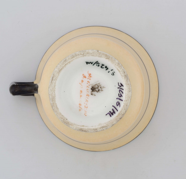 Filiżanka koniczna na pierścieniowej stopie, ucho łamane. Powierzchnia pokryta jednolitym kolorem żółtego ugru, krawędzie konturowane czarnymi paskami, ucho czarne, poniżej wylewu cienka czarna obwódka.
 