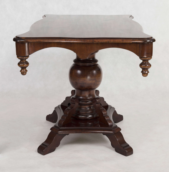 Stół na jednej nodze, blat prostokątny o brzegu falistym obwiedzionym profilowaną listwą. Oskrzynienie wykrojone faliście z brzegiem obwiedzionym odcinkami półwałka zakończonymi wolutowo, w narożnikach dodane toczone sterczynki. Noga tralkowa, profilowana,  na czworobocznym cokole z czterema ozdobnie wycinanymi nóżkami.  