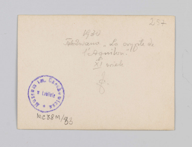 MC/M/38/33/ML - Zdjęcie wykonano w pozycji wertykalnej. Przedstawia Crypte de l'Aquilon będącą w średniowieczu wejściem do opactwa. Na pierwszym planie znajduje się kolumna dzieląca kompozycyjnie zdjęcia na dwie części. Kolumna w stylu romańskim zbudowana na wysokiej plincie. Baza składa się z trochilosa i torusa. Trzon kolumny gładki. Głowica pączkowa, wczesnogotycka, zdobiona mocno uproszczonymi liśćmi akantu (nazwiązuje do stylu korynckiego w architekturze). Abakus w formie odwróconego trapezu. Kolumna podtrzymuje gotyckie sklepienie żebrowe wybudowane w 1103 roku. Po prawej stronie zdjęcia znajdują się schody z prostą metalową balustradą, prowadzące w górę do innych pomieszczeń opactwa. Po lewej stronie zdjęcia widoczny tył sali. 
Na odwrociu fotografii w prawym górnym rogu znajduje się odręczny napis ołówkiem z numerem 