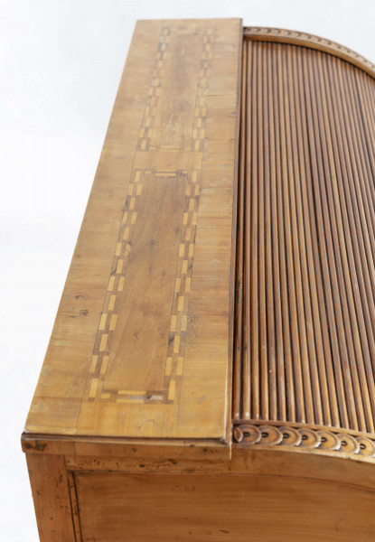 Biurko przyścienne na sześciu nóżkach graniastych zbieżnych. W części dolnej prostokątny prześwit zamknięty tylną ścianą. Po jego bokach po dwie szuflady, powyżej jeszcze trzy. Część górna ćwierćcylindryczna zamykana żaluzją chowaną pod górna płytą powyżej pięciu szufladek, boki zdobione plastycznym ornamentem cekinowym. Lico pokryte fornirem z intarsją ramkową i wzorem arkadkowym. Blat wyłożony skórą cielęcą. Uchwyty szuflad zewnętrznych i żaluzji to nałożone okucia okrągłe z tarczą, szufladki w części górnej mają uchwyty okrągłe z gładką główką.  