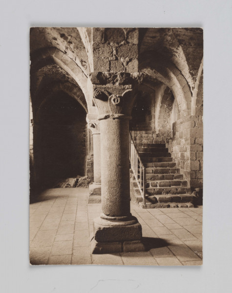 MC/M/38/33/ML - Zdjęcie wykonano w pozycji wertykalnej. Przedstawia Crypte de l'Aquilon będącą w średniowieczu wejściem do opactwa. Na pierwszym planie znajduje się kolumna dzieląca kompozycyjnie zdjęcia na dwie części. Kolumna w stylu romańskim zbudowana na wysokiej plincie. Baza składa się z trochilosa i torusa. Trzon kolumny gładki. Głowica pączkowa, wczesnogotycka, zdobiona mocno uproszczonymi liśćmi akantu (nazwiązuje do stylu korynckiego w architekturze). Abakus w formie odwróconego trapezu. Kolumna podtrzymuje gotyckie sklepienie żebrowe wybudowane w 1103 roku. Po prawej stronie zdjęcia znajdują się schody z prostą metalową balustradą, prowadzące w górę do innych pomieszczeń opactwa. Po lewej stronie zdjęcia widoczny tył sali. 
Na odwrociu fotografii w prawym górnym rogu znajduje się odręczny napis ołówkiem z numerem 