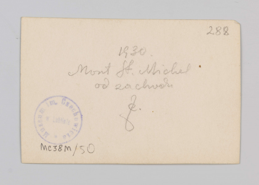 MC/M/38/50/ML - Fotografia w pozycji poziomej. Widok ogólny wzgórza od strony północno zachodniej. Widoczne po lewej zabudowania klasztorne, po prawej górna część fasady kościelnej wraz z wierzą na skrzyżowaniu naw. U dołu po praej na skale kaplica św. Auberta.
Na odwrocie w prawym górnym rogu napis ołówkiem: 