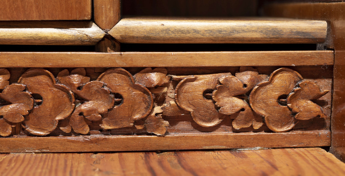 Biurko przyścienne na sześciu nóżkach graniastych zbieżnych. W części dolnej prostokątny prześwit zamknięty tylną ścianą. Po jego bokach po dwie szuflady, powyżej jeszcze trzy. Część górna ćwierćcylindryczna zamykana żaluzją chowaną pod górna płytą powyżej pięciu szufladek, boki zdobione plastycznym ornamentem cekinowym. Lico pokryte fornirem z intarsją ramkową i wzorem arkadkowym. Blat wyłożony skórą cielęcą. Uchwyty szuflad zewnętrznych i żaluzji to nałożone okucia okrągłe z tarczą, szufladki w części górnej mają uchwyty okrągłe z gładką główką.  