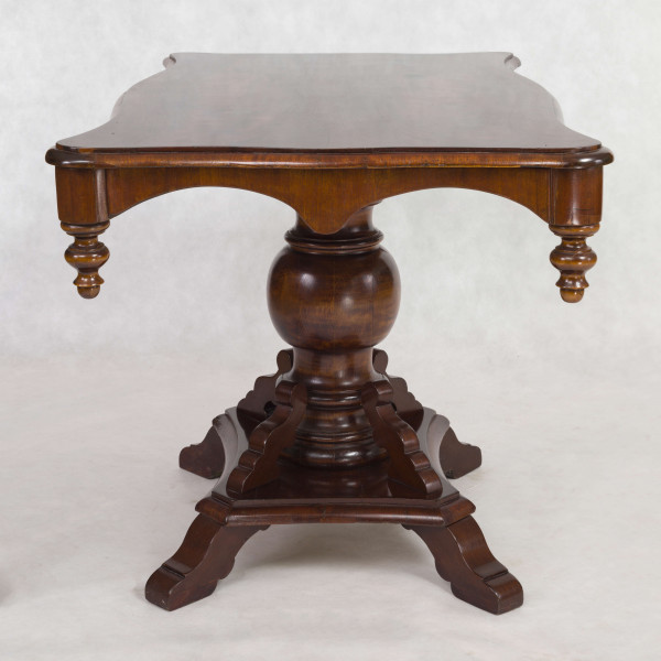 Stół na jednej nodze, blat prostokątny o brzegu falistym obwiedzionym profilowaną listwą. Oskrzynienie wykrojone faliście z brzegiem obwiedzionym odcinkami półwałka zakończonymi wolutowo, w narożnikach dodane toczone sterczynki. Noga tralkowa, profilowana,  na czworobocznym cokole z czterema ozdobnie wycinanymi nóżkami.  