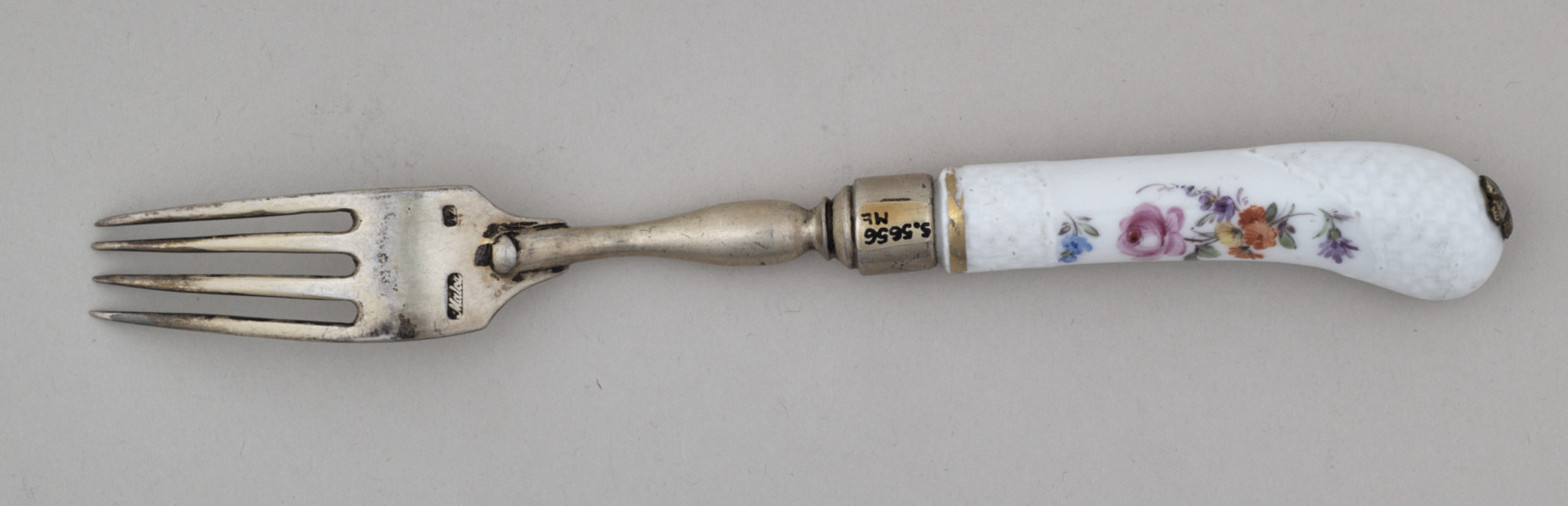 Widelec śniadaniowy, czterozębny. Zęby wygięte, zwężające się przy zakończeniu. Trzonek z nakładką ze srebra złoconego z białej porcelany