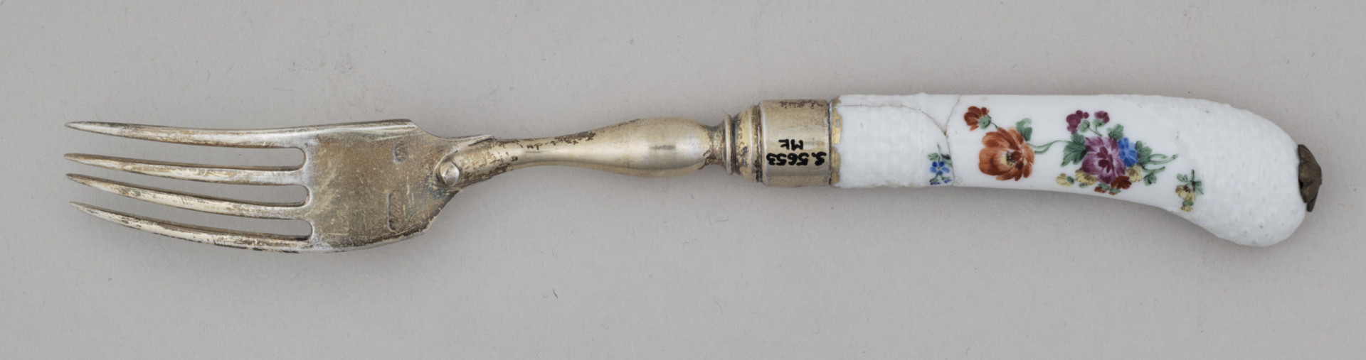 Widelec śniadaniowy, czterozębny. Zęby wygięte, zwężające się przy zakończeniu. Trzonek z nakładką ze srebra złoconego z białej porcelany