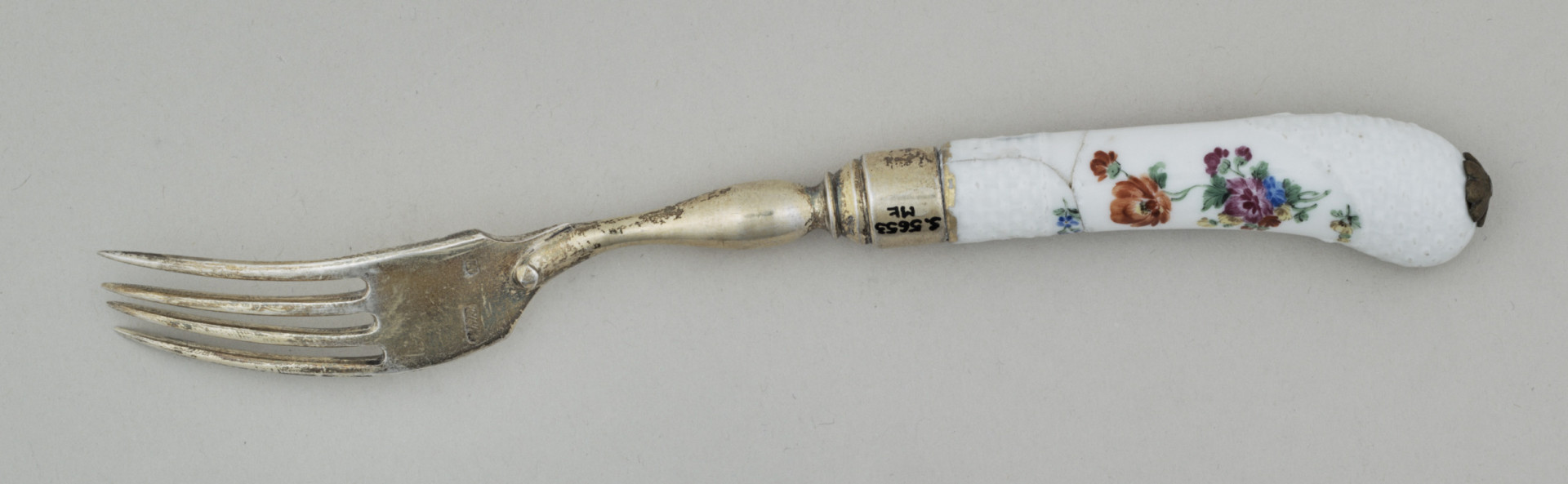 Widelec śniadaniowy, czterozębny. Zęby wygięte, zwężające się przy zakończeniu. Trzonek z nakładką ze srebra złoconego z białej porcelany