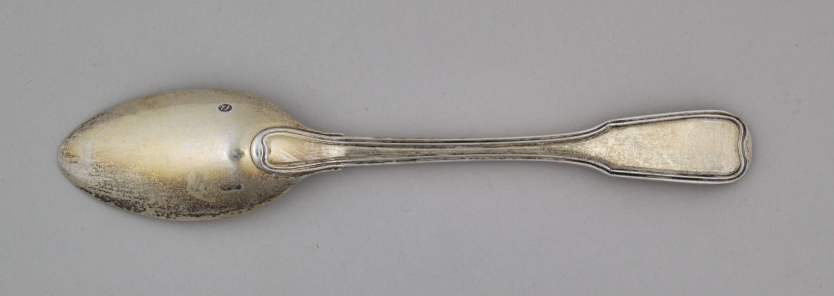 Nieduża łyżka obiadowa o głębokiej owoidalnej czarce. Trzonek płaski, lekko wygięty, rozszerzający się przy zakończeniu, ozdobiony przy krawędzi z obu stron podwójnym profilowaniem
