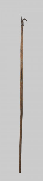 bosak rybacki - Ujęcie z przodu; Bosak rybacki wykuty z płaskiego pasa metalu, którego jedną połowę po częściowym rozcięciu wzdłużnym pozostawiono po zwężeniu jako pionowy szpic, a drugą zagięto w dół w półokrąg i również zwężono w szpic. Koniec tego pasa przechodzi na dole w okrągłą obejmę do nasadzania na drzewce.