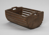 Skrzynka do przechowania i przenoszenia przynęty - Ujęcie ze skosu z lewej; Drewniana skrzynka w formie niecki, w przekroju poprzecznym – półkolista. Dłuższe boki i podstawę wykonana z płaskich klepek przytwierdzonych do krótszych, pełnych boków zaopatrzonych w uchwyty, Klepki do boków przybite gwoździkami.