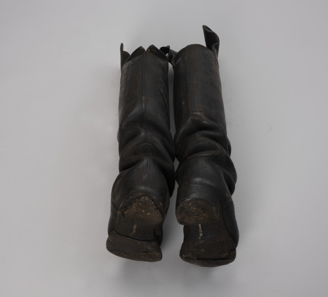 tłok pieczętny - Ujęcie z tyłu; Para butów rybackich o wysokich cholewach zszytych z dwóch kawałków skóry. Drewniane podeszwy są podbite grubą, barwioną na kolor czarny, sztywną, prawdopodobnie impregnowaną tłuszczem, skórą za pomocą gwoździków.