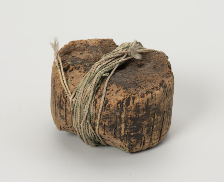 węda pływająca - Ujęcie z boku; Węda pływająca składająca się z okrągłego pływaka z otworem w środku, wykonanego z korka, na powierzchni którego widać liczne obłupienia. Do pływaka przywiązana jest bawełniana nić.