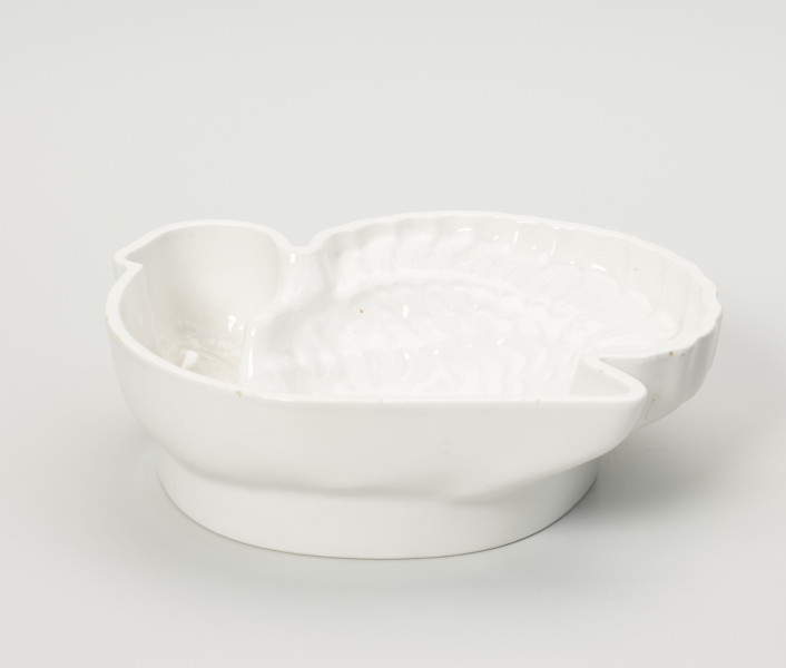 forma ceramiczna - Ujęcie z przodu; Fajansowe, szkliwione jednolicie na biało naczynie w kształcie indyka. Realistyczna postać ptaka odwzorowana w postaci wgłębnego wzoru. Dno z wyraźnie wyodrębnioną stopką w części środkowej.