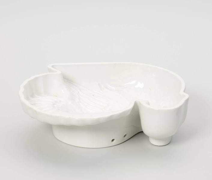 forma ceramiczna - Ujęcie z tyłu; Fajansowe, szkliwione jednolicie na biało naczynie w kształcie indyka. Realistyczna postać ptaka odwzorowana w postaci wgłębnego wzoru. Dno z wyraźnie wyodrębnioną stopką w części środkowej. Na stopce dwa otwory dające możliwość powieszenia naczynia na ścianie lub w kredensie.