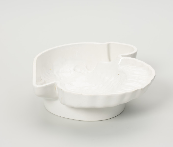 forma ceramiczna - Ujęcie z tyłu; Fajansowe, szkliwione jednolicie na biało naczynie w kształcie indyka. Realistyczna postać ptaka odwzorowana w postaci wgłębnego wzoru. Dno z wyraźnie wyodrębnioną stopką w części środkowej.