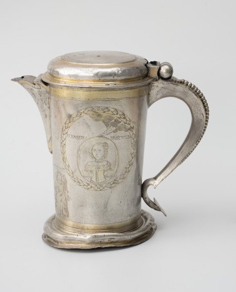 dzban na wino komunijne - Ujęcie z prawej; Cylindryczny dzban o korpusie lekko zwężającym się ku dołowi, wsparty na wysklepionej stopie i nakryty spłaszczoną pokrywą na zawiasie, z utrąconym uchwytem. Wylew trójkątny, faliście wycięty, częściowo przesłonięty. Esowato wygięte ucho ozdobione perełkowaniem i zakończone płaską tarczką. Korpus dzbana zdobi grawerowana i złocona dekoracja. W wieńcu z liści laurowych medalion portretowy trzymany przez wysuwającą się z obłoków rękę Boga. W owalu ukazana jest młoda kobieta o włosach gładko zaczesanych nad czołem i ujętych w koczek, z drobnymi loczkami przy twarzy, w odsłaniającej ramiona sukni z bufiastymi rękawami, na jej szyi okrągły medalion i naszyjnik z pereł. Zgodnie z podpisem portret przedstawia Elisabethę Brüsewitz.