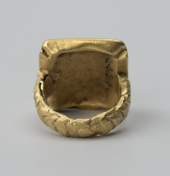 pierścień z Pęzina - Ujęcie spodu; Pierścień zbudowany z obrączki i dużej prostokątnej tarczki. Zewnętrzna część obrączki, lekko wypukła. Tarczka prostokątna, zbliżona do kwadratu, o fasetowanych bokach.