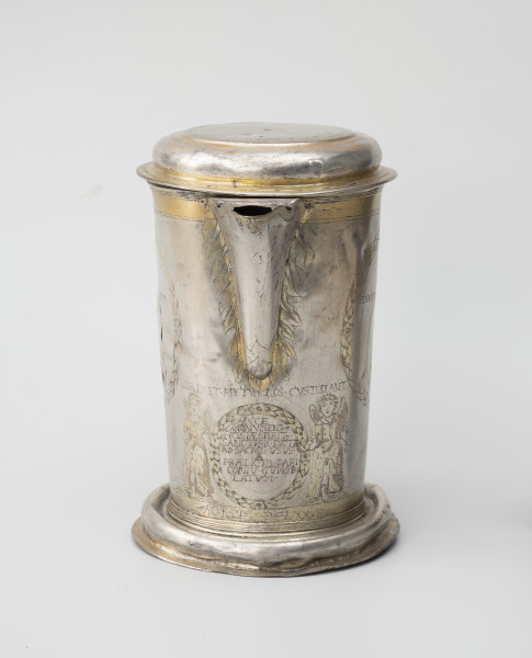 dzban na wino komunijne - Ujęcie z przodu; Cylindryczny dzban o korpusie lekko zwężającym się ku dołowi, wsparty na wysklepionej stopie i nakryty spłaszczoną pokrywą. Wylew trójkątny, faliście wycięty, częściowo przesłonięty. Korpus dzbana zdobi grawerowana i złocona dekoracja. Wylew w otoczeniu płomieni, poniżej para aniołów trzymających wieniec laurowy z inskrypcją fundacyjną. SIMPLEX .ET. RECTVM NOS.CVSTODIANT | HOCCE. |  MONVMENTVM |  ECCLESIAE SPIRIT SANCTI.SIC. DICTAE | AD.SACROS. VSVS. |  A  | PRAEDICTO. PARI |  CONIV. GVMOB: |  LATVM | A.O.R.M DCLXXVII