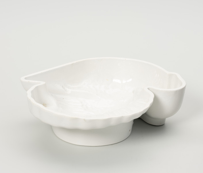 forma ceramiczna - Ujęcie z przodu; Fajansowe, szkliwione jednolicie na biało naczynie w kształcie indyka. Realistyczna postać ptaka odwzorowana w postaci wgłębnego wzoru. Sygnatura firmy na stemplu umieszczonym w centralnej części na dnie naczynia. Dno z wyraźnie wyodrębnioną stopką w części środkowej. Na stopce dwa otwory dające możliwość powieszenia naczynia na ścianie lub w kredensie.