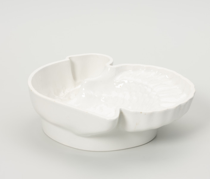 forma ceramiczna - Ujęcie z boku; Fajansowe, szkliwione jednolicie na biało naczynie w kształcie indyka. Realistyczna postać ptaka odwzorowana w postaci wgłębnego wzoru. Sygnatura firmy na stemplu umieszczonym w centralnej części na dnie naczynia. Dno z wyraźnie wyodrębnioną stopką w części środkowej. Na stopce dwa otwory dające możliwość powieszenia naczynia na ścianie lub w kredensie.