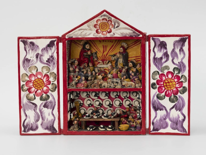 retablo - Ujęcie z przodu; Jasna, bogato dekorowana kolorowymi wzorami florystycznymi, prostopadłościenna, wewnątrz dwupoziomowa skrzynka (kapliczka) z dwuskrzydłowymi drzwiczkami, zwieńczona trójkątną koroną. Na wyższym poziomie pokazano Narodzenie Dzieciątka Jezus, gdzie wykonane z pasty ziemniaczanej i gipsu, polichromowane postacie Marii, Józefa i malutkiego Jezusa ustawiono na podwyższeniu. Bezpośrednio za Świętą Rodziną znajdują się zwierzęta: osioł i krowa. Poniżej głównych (nieco większych od pozostałych) figur zaprezentowano miejscową ludność (kobiety, mężczyzn i dzieci) w pozycji modlitewnej – większość klęczy z dłoniami złożonymi i skierowanymi ku Dzieciątku. Pierwszy rząd wypełniają najmniejsze figurki zwierząt hodowlanych: kóz, owiec, cieląt, jagniąt, krów, kur, źrebiąt oraz kota. Tło przedstawienia składa się z dwóch różnych dekoracji. Po obu bokach zastosowano wzór kropkowy (wielokolorowy) na białym tle, natomiast centralnie za postaciami namalowano usytuowane nisko na horyzoncie czerwone słońce na żółtym tle. Dolne piętro przedstawia scenę rodzajową: sprzedawcę kapeluszy w sklepie lub na targu w towarzystwie miejscowej ludności, instrumentów muzycznych i prawdopodobnie psa. Różowe tło wypełniono trzema rzędami figurek przedstawiających biało-czarne kapelusze typu panama.