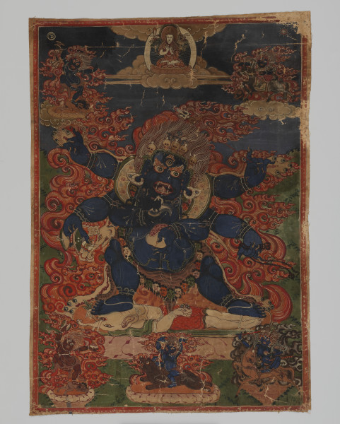 thanka; Mahākāla depczący po ciele Ganeśy - Ujęcie z przodu; Nieobszyty i nieoprawiony obraz bóstwa na bawełnianym płótnie z sześcioramiennym Mahākālą depczącym po ciele słoniogłowego Ganeśy w centrum. Duża postać ciemnoniebieskiego Mahākāli wypełnia całą kompozycję. Ma pękaty brzuch, czerwone, stojące włosy, dodatkowe, trzecie oko na czole, brwi w postaci jaskrawych płomieni oraz otwarte usta, w których uwidoczniono zęby, język oraz cztery kły. Ubrany jest w przepaskę ze skóry tygrysa i koronę z pięciu ludzkich czaszek na głowie (sanskryt pancakapala). Nad środkową czaszką widoczny jest niebieski wąż i połówka dordży (sanskryt wadżra) wieńcząca płonący klejnot. Z jego szyi zwisa bardzo długi, sięgający do kostek naszyjnik w formie girlandy ze ściętych ludzkich głów (sanskryt muṇḍamālā, kapālamala). Ramiona i brzuch oplata mu zielony wąż. Mahākāla ma długie i ostre – szponiaste – paznokcie. W górnych dłoniach trzyma okrągły różaniec z czaszek - w prawej i trójząb (tybetański rtse-gsum, sanskryt triśūla) - w lewej; w środkowych dłoniach: obrzędowy bębenek damaru w prawej, nadprzyrodzoną broń - lasso lub pętlę (w sanskrycie nazywaną pāśa) w lewej; natomiast w dolnych: w prawej mały, ręczny nóż w kształcie półksiężyca (nepalski kartika, sanskryt kartari), a w lewej naczynie z ludzkiej czaszki (tybetański kapala, sanskryt kapāla) wypełnione ludzkimi organami. Na przedramionach, przegubach dłoni i kostkach ma bransolety – prawdopodobnie z ludzkich kości – oplecione małymi, kolorowymi wężami. Z jego uszu zwisają duże, bogato zdobione kolczyki z błękitnymi klejnotami. Pośrodku brzucha znajduje się zawieszona na cienkim łańcuszku, oplecionym wokół klatki piersiowej, zawieszka najprawdopodobniej przedstawiająca koło życia. Leżący pod stopami Mahākāli Ganeśa ma białe ciało, które od pasa w dół ubrane jest w czerwoną, połyskującą tkaninę. Jego ramiona oplata zielona szarfa, natomiast na torsie widać sznury zielonych korali lub klejnotów. W prawej dłoni trzyma miskę z czaszki wypełnioną klejnotami (?), w lewej bliżej nieokreśloną roślinę, którą wkłada do pyska. Główne postacie umieszczono na lotosowej podstawie otoczonej jaskrawymi płomieniami. W górnej części kompozycji, w obłokach, pośrodku, widoczny jest górujący nad pozostałymi postaciami Lodothaya w czerwonej czapce – nauczyciel szkoły Nyingma (tzw. szkoła, zakon Czerwonych Czapek, najstarsza ze szkół buddyjskich w Tybecie). Siedzi on na lotosowym tronie w pozycji lotosu (sanskryt padmāsana), a jego ręce ułożone są w geście nauczania (sanskryt dharmacakra). Ma nimb oraz srebrną mandorlę. Po obu jego stronach widoczny jest kwiat lotosu. Po lewej stronie na lotosie znajduje się księga z naukami buddyjskimi. W górnym i dolnym lewym rogu malowidła znajdują się dwie postacie depczące po ludzkich, nagich ciałach. Są to przedstawienia gniewnej manifestacji Awalokiteśwary (tybetański Chenrezig, sanskryt Avalokiteśvara). Wyglądem przypominają Mahākālę: mają trzy oczy, stojące, płomienne włosy, na głowach koronę z pięciu czaszek oraz przepaskę z tygrysiej skóry na biodrach. Górna postać jest ciemnoniebieska, w prawej ręce trzyma obrzędowy bębenek damaru. Dolna jest bordowa, w prawej ręce ma bębenek, a w lewej misę z czaszki wypełnioną ludzkimi organami. Obie przedstawiono na tle jaskrawych płomieni i lotosowej podstawie. W górnym i dolnym prawym rogu kompozycji znajdują się kolejne dwie postacie wyglądem podobne do Mahākāli. Górna, siedząca na ciemnym koniu to prawdopodobnie Dugon Trakshad – główny towarzysz (pomocnik) Mahākāli. Ubrany jest w czerwoną szatę i buty. W prawej dłoni trzyma trójząb, a w lewej misę z czaszki. Pod kopytami konia widoczne jest nagie, ludzkie ciało. Koń i jeździec umieszczeni są na białym obłoku w otoczeniu jaskrawych płomieni. Dolna postać to bogini Palden Lhamo (sanskryt Śridewi) – służebnica Mahākāli. Nad jej koroną z pięciu czaszek znajduje się ozdoba z pawich piór. Siedzi na nieujeżdżonym ośle – kiangu tybetańskim. W uniesionej prawej ręce trzyma dordże osadzone na sandałowym trzonie. W lewej dłoni na wysokości serca ściska wypełnioną krwią misę z czaszki dziecka zrodzonego z kazirodczego związku. Z jej prawego ucha wystaje lew, a z lewego wąż. Osioł zwraca łeb w stronę bogini, która ma na sobie czarną, jedwabną szarfę, przepaskę z tygrysiej skóry i naszyjnik (girlandę) ze świeżo ściętych głów ludzkich. Siodło wierzchowca zrobione jest z ludzkich skór, przymocowano do niego parę czarno-białych kości oraz magiczną kulę ze sznura widoczną przy tylnej nodze osła obok oka. Do pasa ma przymocowaną sakwę z chorobami oraz czerwoną tabliczkę do rzucania zaklęć. Przedstawiona jest na tle ciemnych (brązowych) płomieni. Pośrodku, w dolnej części kompozycji umieszczono siedzącą na brunatnym niedźwiedziu postać podobną do Mahākāli. Jest to prawdopodobnie Kszetrapala (sanskryt Kṣetrapāla). W prawej dłoni trzyma nóż kartika, w lewej misę z czaszki wypełnioną ludzkimi organami. Przedstawiony na lotosowej podstawie w otoczeniu jaskrawych płomieni. Dodatkowo w prawym górnym rogu kompozycji zauważyć można małe słońce, a w lewym zamknięty w okręgu księżyc. Tło malowidła stanowi wyobrażenie nieba (góra) oraz ziemi (dół). Kompozycja wykończona została wąską, czerwoną ramą. Odznacza się bogactwem detali i starannością wykonania. Wydaje się kanoniczna. Na jej odwrocie znajduje się zapisany czerwonym tuszem tekst w jęz. tybetańskim. Widoczne są ślady maszynowego szycia (wewnątrz czerwonej ramki), liczne przetarcia (awers) oraz odbarwienia (rewers). Być może thanka została odpruta od materiałowej bordiury.