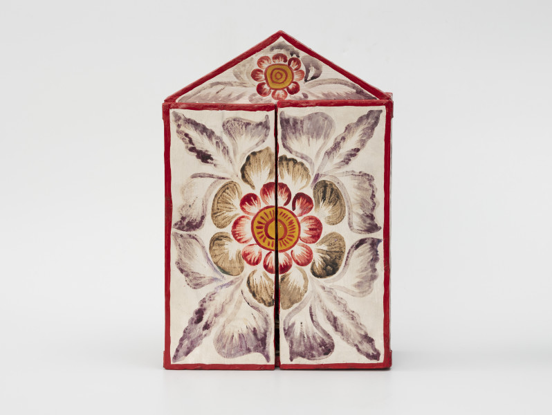 retablo - Ujęcie z przodu; Jasna, bogato dekorowana kolorowymi wzorami florystycznymi, prostopadłościenna, skrzynka (kapliczka) z dwuskrzydłowymi drzwiczkami, zwieńczona trójkątną koroną.