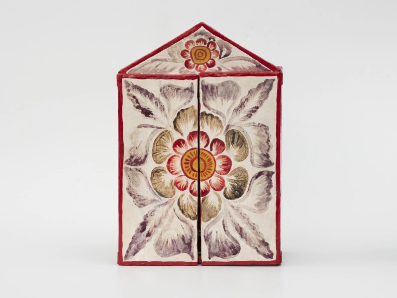 retablo - Ujęcie z przodu; Jasna, bogato dekorowana kolorowymi wzorami florystycznymi, prostopadłościenna, skrzynka (kapliczka) z dwuskrzydłowymi drzwiczkami, zwieńczona trójkątną koroną.