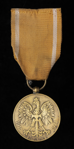 Medal Pamiątkowy Za Wojnę 1918-1921 - Ujęcie z przodu; Medal ma kształt okrągły. Na awersie medalu umieszczono godło państwowe (według wzoru z 1927) – orzeł w koronie, na piersi którego widnieje – zawieszony na szyi – Krzyż Orderu Wojennego Virtuti Militari. Po obu stronach godła, tuż pod szponami, znajdują się rozpisane na okręgu daty: 1918 i 1921. Zawieszenie z przylutowanego uszka o kształcie beczułkowatym i przewleczonego kółeczka. Wstążka nieregulaminowa - żółta z białymi paskami.