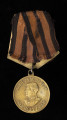 medal Za zwycięstwo nad Niemcami w Wielkiej Wojnie Narodowej 1941-1945 - Ujęcie z przodu; Medal jest okrągły, z czarno-pomarańczową wstążką na stelażu, z baretką wykonaną z tego samego materiału. Na awersie znajduje się wizerunek Józefa Stalina w lewym profilu, otoczony napisem w języku rosyjskim: НАШЕ ДЕЛО ПРАВОЕ | МЫ ПОБЕДИЛИ.