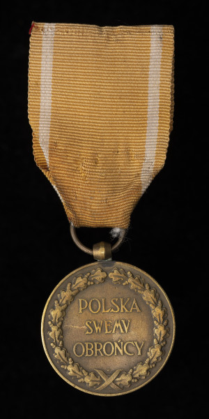 Medal Pamiątkowy Za Wojnę 1918-1921 - Ujęcie z tyłu; Medal ma kształt okrągły. Na rewersie medalu umieszczony został wieniec z liści dębowych, wewnątrz którego widnieje rozpisany w kolumnie napis: POLSKA SWEMU OBROŃCY. Między wstążkami przewiązującymi wieniec wybity znak Mennicy Państwowej. Zawieszenie z przylutowanego uszka o kształcie beczułkowatym i przewleczonego kółeczka. Wstążka nieregulaminowa - żółta z białymi paskami.