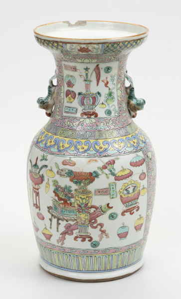 wazon typu famille rose - ujęcie z tyłu; Porcelanowy wazon zdobiony wielobarwną dekoracją naszkliwną w pastelowych odcieniach z przewagą różu w typie famille rose. Kształt gruszkowaty, szyja szeroka zakończona rozszerzającym się wylewem, w którym widoczny jest w tyle półokrągły ubytek. Wazon bogato zdobiony licznymi motywami dekoracyjnymi. W jego górnej części po bokach znajdują się dwa uchwyty w formie stylizowanych lwów chińskich w kolorze pastelowej zieleni. Brzeg wylewu zdobiony dookolnie i motywem stylizowanego lotosu o czerwonym kwiecie, żółtych i zielonych liściach na białym tle oraz zgeometryzowanym wzorem roślinnym w kolorach zielonym i różowym na żółtym tle. Szyję oddzielono od brzuśca biegnącymi dookolnie wzorami: ornamentem meandrycznym o różowej, żółtej i seledynowej barwie oraz znajdującym się pod nim motywem grzyba nieśmiertelności w niebieskim, żółtym, czerwonym i seledynowym kolorze. Brzusiec oraz szyję zdobią czworoboczne pola (rezerwy) o seledynowych bordiurach wypełnione tzw. motywem Stu Antyków (Hundred Antiques/Hundred Treasures) na białym tle. Ułożono je na na szyi oraz na brzuścu. Pola wypełniają przedmioty i rośliny w dość nieformalnym układzie. Na szyi wyodrębnić można: różnorodne wazy (z przykrywkami oraz bez, na stojaku oraz bez), dyski z jadeitu, podwójną tykwę, z której unosi się smużka dymu oraz inne niezidentyfikowane przedmioty. Na brzuścu pokazano: wazę z kwiatami na stojaku, akwarium na stojaku, różnorodne wazy, donicę z miniaturową rośliną na stojaku, naczynie na wysokim stojaku oraz inne niezidentyfikowane przedmioty i rośliny. Dół wazonu ozdobiony dookolnie geometrycznym motywem w postaci pionowych żółtych i różowych pasków na seledynowym tle. Na brzuścu widoczne są ślady klejenia.
