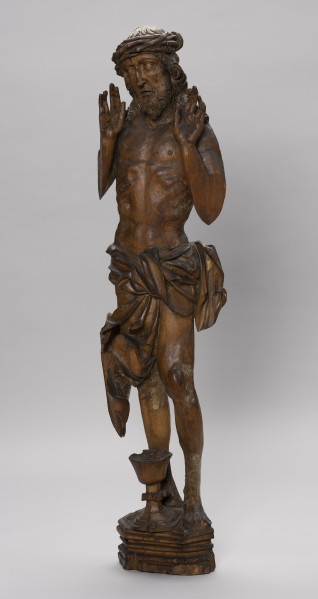 figura ołtarzowa - Ujęcie ze skosu z prawej; Figura Chrystusa stojącego frontalnie na cokole prezentującego rany doznane podczas Ukrzyżowania. Szczupłe ciało Chrystusa o poprawnie oddanych szczegółach anatomicznych okryte w partii bioder długą chustą przewiązaną z przodu o krańcach plastycznie pofałdowanych i powiewających na boki. Dłonie uniesione przy twarzy wnętrzami do widza z charakterystycznym układem długich palców z przerwą między palcem serdecznym a środkowym. Na ciele werystycznie oddane rany w formie otworów w dłoniach i stopach oraz głęboko wybranej rany na boku. Na głowie szeroka korona cierniowa spleciona z gałęzi. Falujące długie włosy opadają puklami na ramiona. Pociągła twarz o regularnych rysach i spokojnym wyrazie, z dużymi oczami spoglądającymi na wprost. Od górnych kącików ust wąsy opadają do krótkiej spiczastej brody zakończonej dekoracyjnym puklem. Na wysokim wielobocznym cokole o profilowanych ściankach, przed Chrystusem ustawiony jest kielich z wydatnym nodusem. Rzeźba przyścienna z drążeniem w partii bioder i pleców. Nogi i ręce poniżej barków opracowane pełnoplastycznie. Powierzchnia rzeźby gładka. Śladowe ilości polichromii i zaprawy gruntowej. Ubytki drewna w partii przedramion, małego palca lewej dłoni, palców lewej stopy i w cokole.