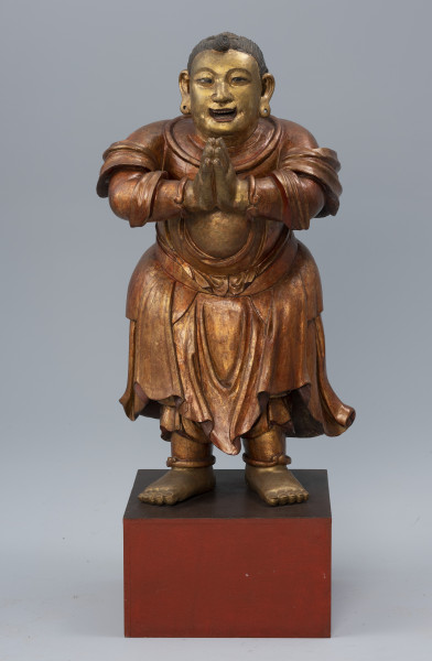 pielgrzym Shancai Tongzi (?) wraz z wypełnieniem - ujęcie z przodu; Monumentalna, drewniana, złocona rzeźba postaci męskiej w pozie adoracji przedstawia prawdopodobnie młodego pielgrzyma. Postać stoi na postumencie z rękami wyciągniętymi przed siebie i dłońmi złożonymi w pełnym szacunku geście. Ma pogodny wyraz twarzy, lekko uniesione brwi, duże, brązowe oczy, podłużne uszy i otwarte, lekko uśmiechnięte usta z widocznym uzębieniem. W jego policzkach zaznaczono dołki, natomiast w płatkach usznych wydrążono niewielkie otwory. Gładko zaczesane czarne włosy. Pielgrzym ubrany jest w długie, kilkowarstwowe, sięgające za kolana szaty, natomiast z jego ramion i rąk opada tkanina w formie szala. Na jego obu nadgarstkach i kostkach widoczne są bransolety. Stopy ma nagie.